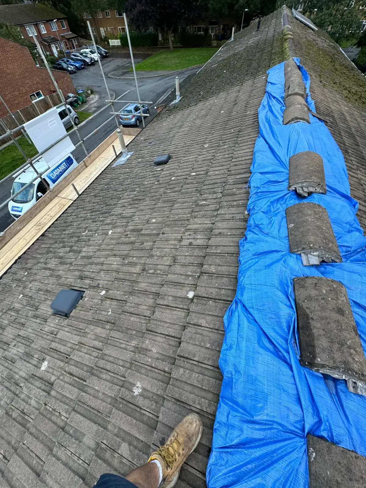 A man laying on top of a roof next to a blue tarp.